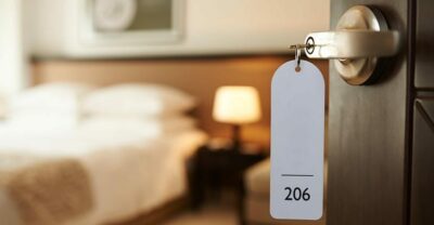 Opened door of hotel room 206 with key in the lock in handle bed and nightstand in in background.