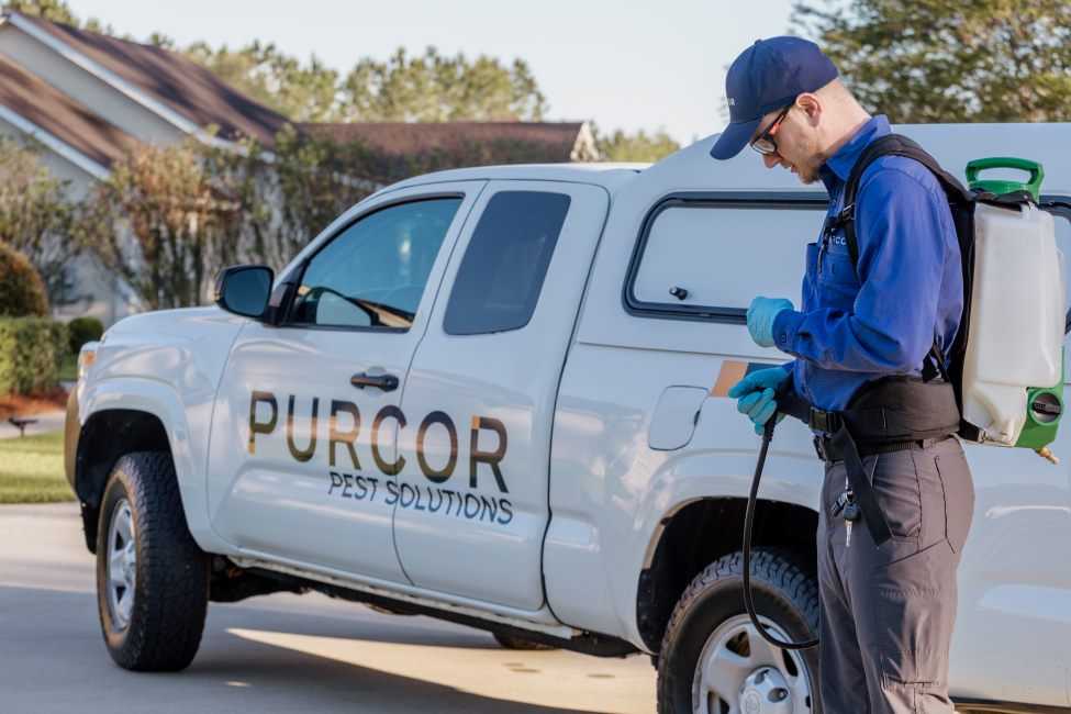 A pest control technician looks at his equipment in front of his PURCOR-branded truck