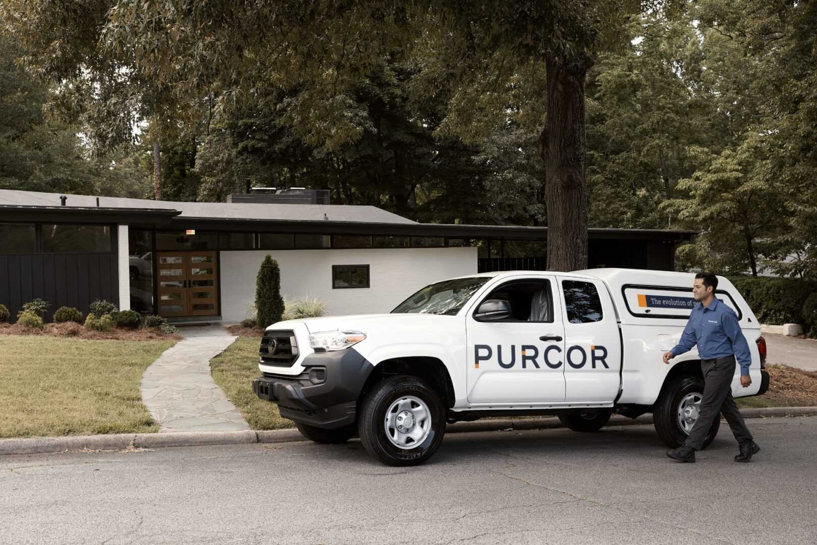 A PURCOR Pest Solutions technician walking to the branded truck parked in front of a home.