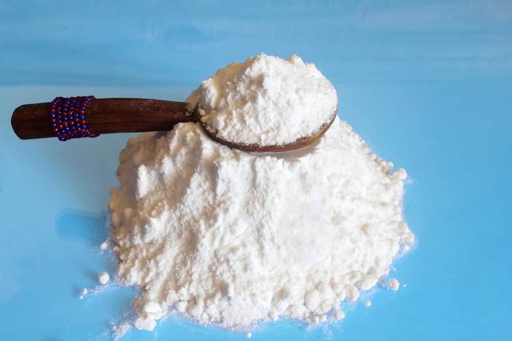A pile of white powder, possibly boric acid used to get rid of roaches, sits on a blue surface with a wooden spoon decorated with blue and red beads resting on top.