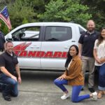 Ten adults pose for a group photo in front of a white pickup truck with “Standard” written on the side, representing Standard Pest Control. Some are standing while others kneel, with trees visible in the background, capturing a moment of camaraderie in Washington.